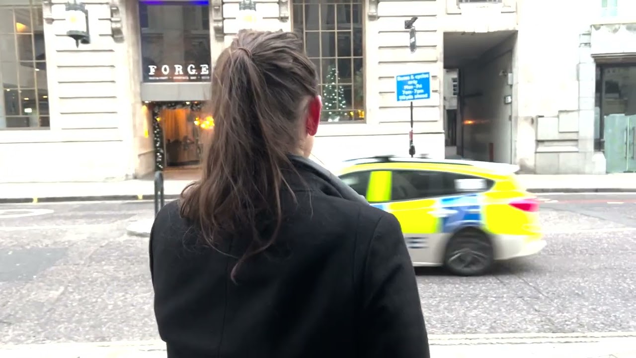 A woman with a ponytail seen from behind on a London street as a police car passes